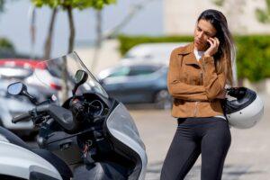A woman on her phone beside her bike, wondering if insurance will cover a motorcycle accident.