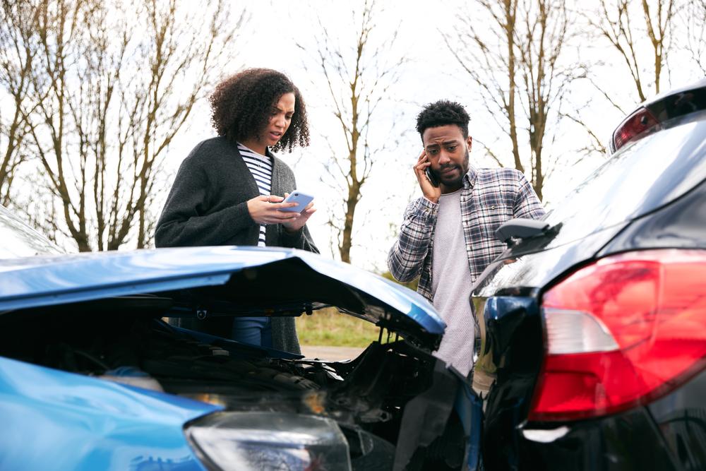 Two people on the side of the road after an auto collision, with people nearby interested in learning about the top three causes of car accidents in Stamford, Connecticut