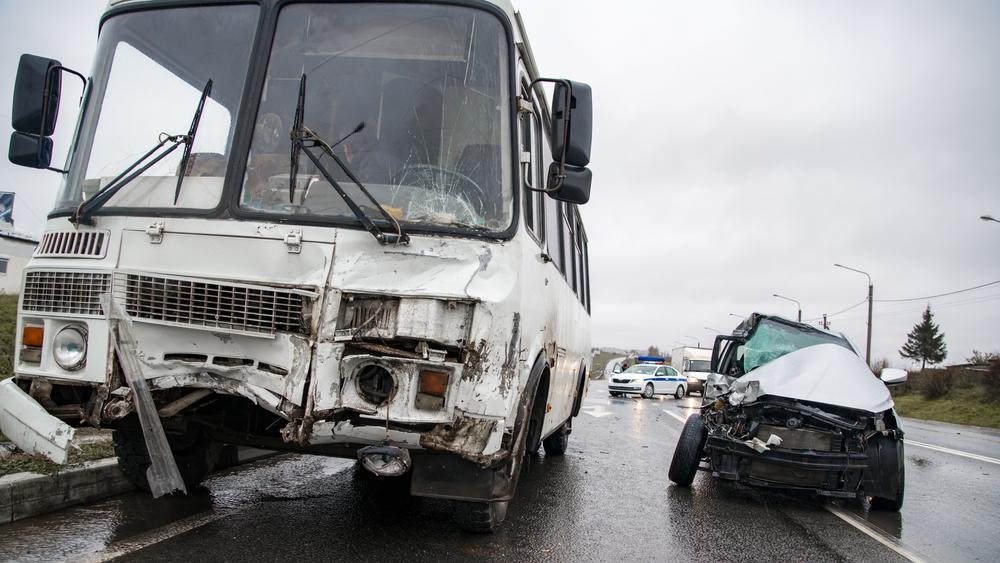 A damaged bus and car sit next to one another in a parking lot after a collision.